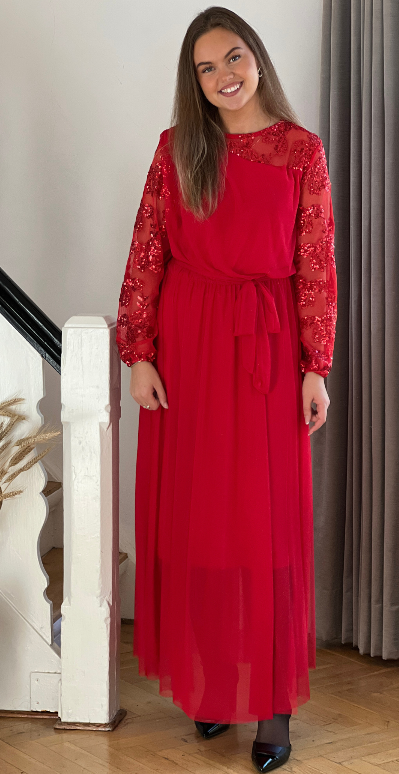 Kvinde i rød Nash kjole i chiffon med pailletter på ærmerne og bindbånd i taljen, set forfra.
