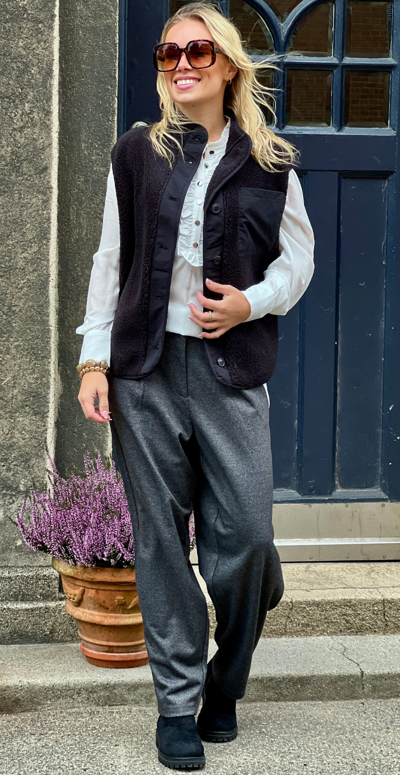 Kvinde set forfra i grå Heika bukser fra LikeLondon.com kombineret med hvid skjorte og sort vest.