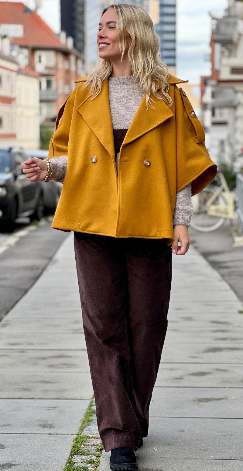 Kvinde i sennepsgul Cleo kort poncho jakke med knapper forfra fra LikeLondon.com.