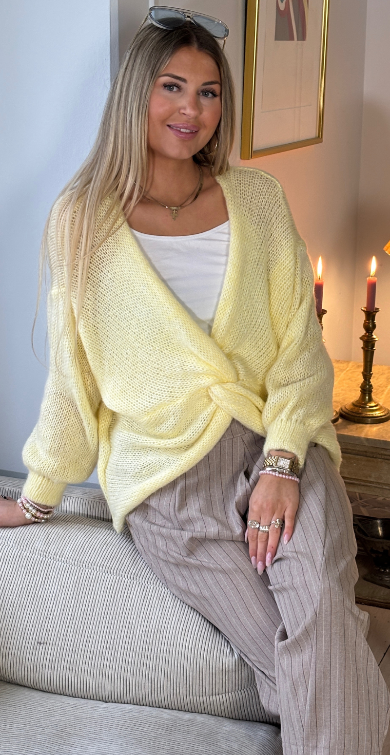 Zinka strik med lange ærmer og knude foran gul LikeLondon