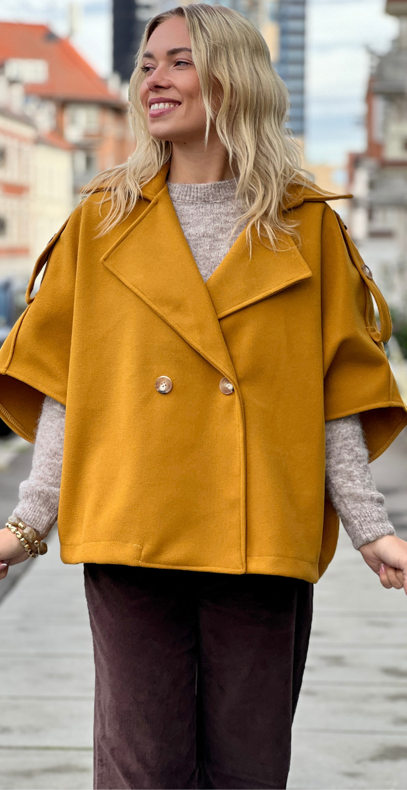 Kvinde i sennepsgul Cleo kort poncho jakke fra LikeLondon.com med knapper forfra.