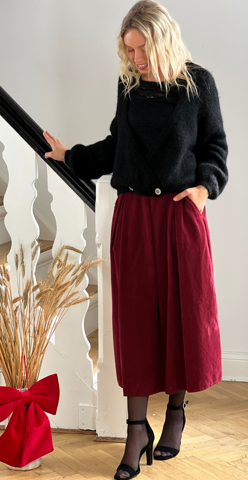 Kvinde i sort Kitty strikcardigan med wrapeffekt og vinrøde bukser set forfra.